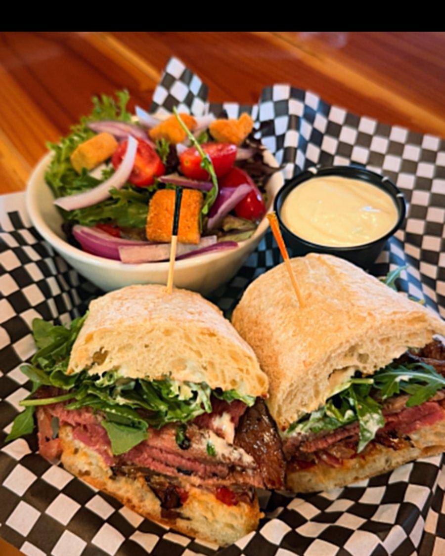 Prime rib baguette sandwich with arugula and a side salad